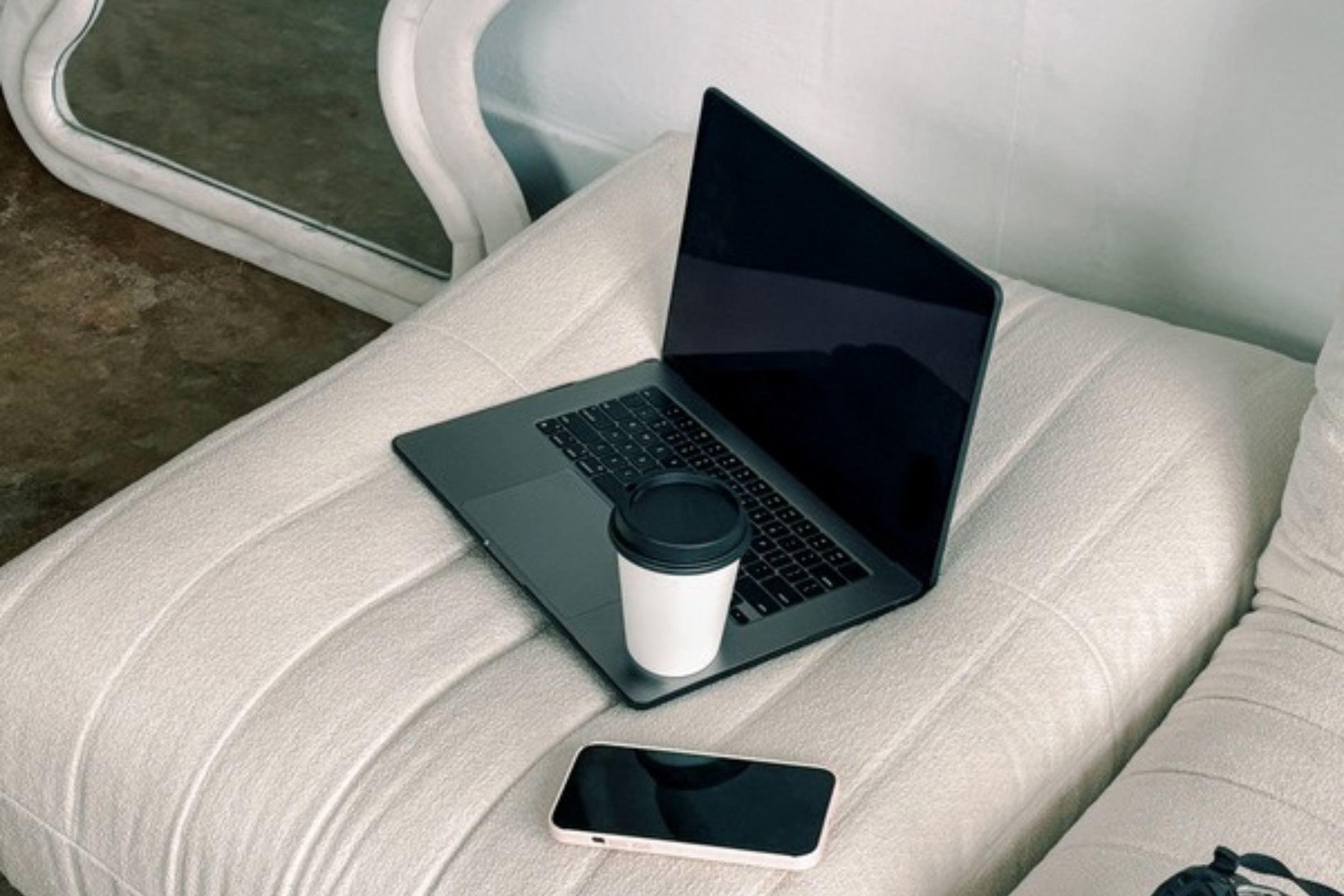 Laptop, smartphone and coffee cup on a cream cushion in a bright home workspace, ready for making Instagram carousels with AI.
